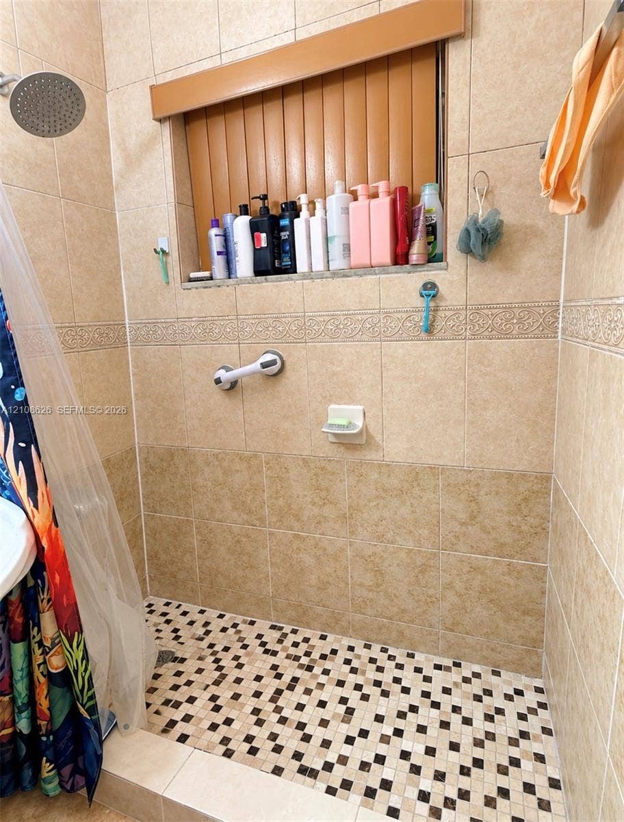 971 NE 156th Terrace, North Miami Beach, FL 33162 Walk-in shower enclosure featuring floor-to-ceiling tile, a decorative tile border, a built-in recessed shelf, and a mosaic-tile shower floor