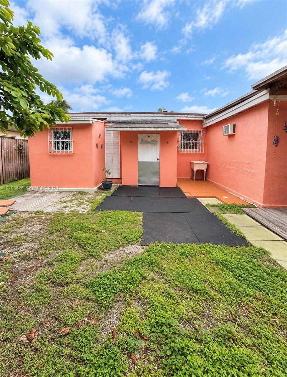 971 NE 156th Terrace, North Miami Beach, FL 33162 Stucco exterior with metal security window grilles, a metal-paneled entry door, and a built-in outdoor utility basin