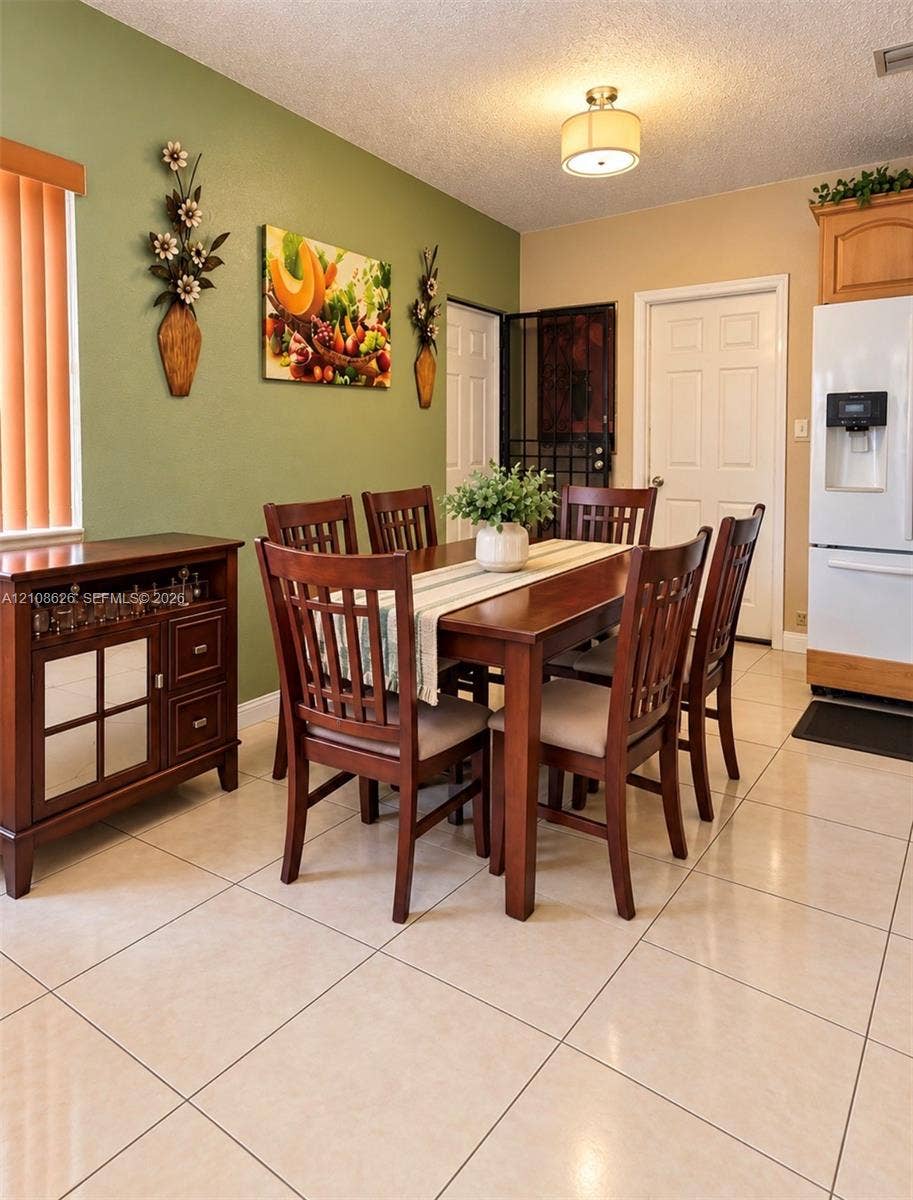 971 NE 156th Terrace, North Miami Beach, FL 33162 Dining area featuring polished light-toned floor tiles, a drum-style ceiling light fixture, wood cabinetry, and vertical blind window treatments
