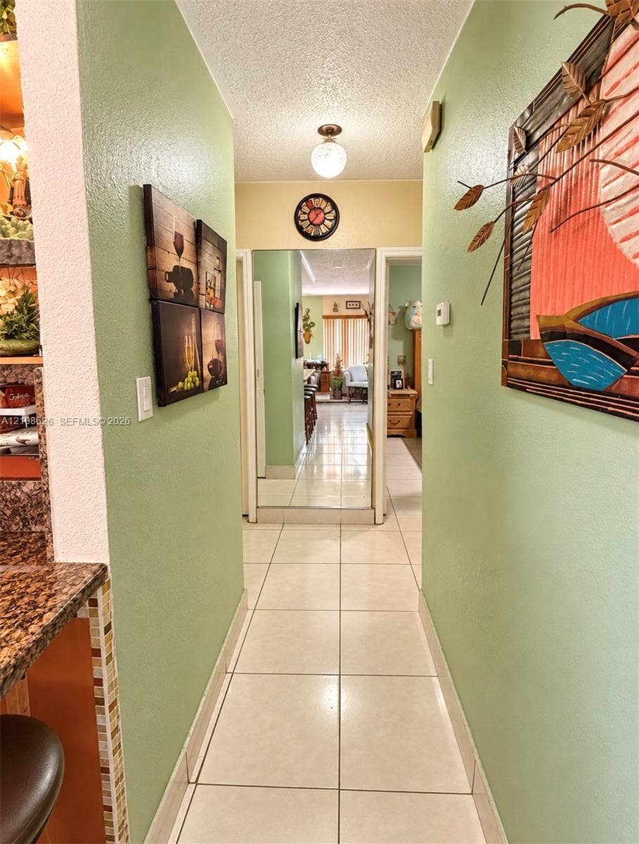 971 NE 156th Terrace, North Miami Beach, FL 33162 Interior hall featuring large-format ceramic tile flooring, full-length mirror paneling, and flush-mount overhead lighting