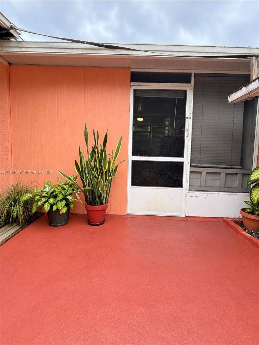 971 NE 156th Terrace, North Miami Beach, FL 33162 Covered patio featuring a solid-surface floor, vertical panel siding, and a screen door with a transom window