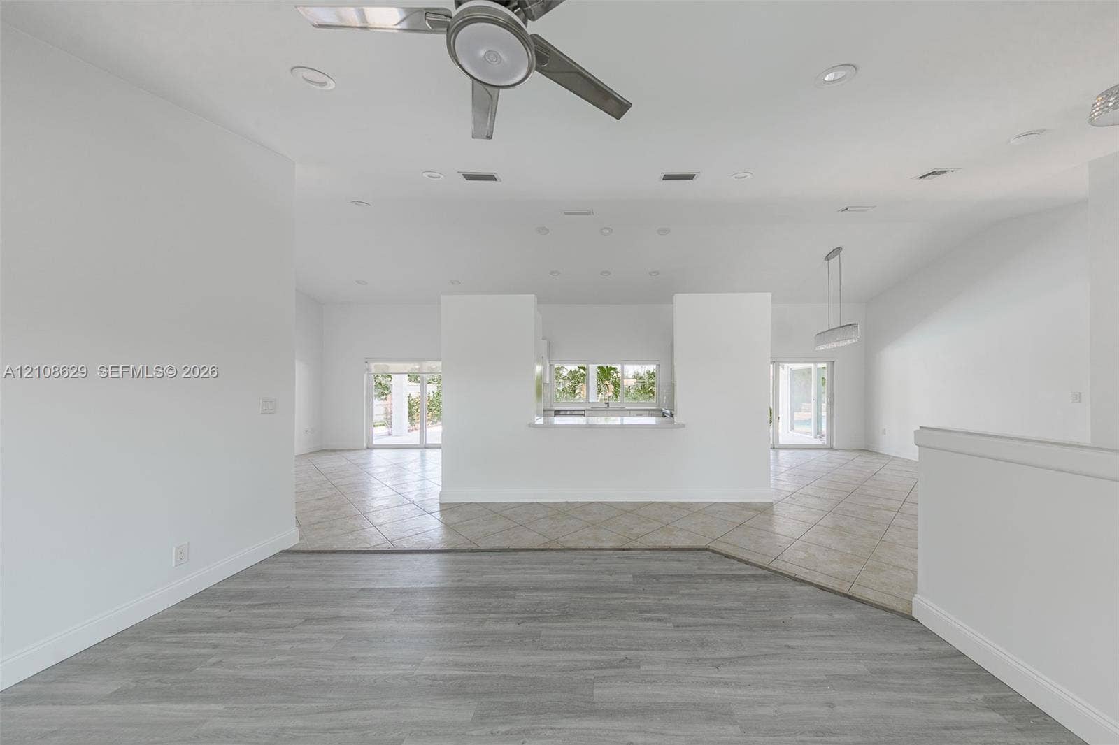 Open-concept interior featuring wood-finish flooring, ceramic tile flooring, a central partition wall with a pass-through counter, recessed lighting, and a ceiling fan