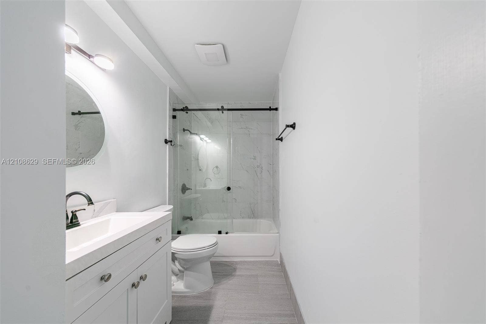 Bathroom featuring a white vanity with a rectangular sink, stone-finish surround shower with a glass sliding door, matte black hardware, and wood-finish tile flooring