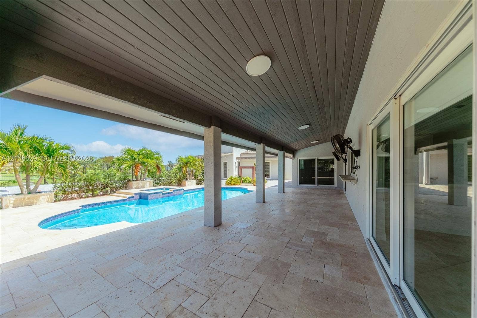 Covered patio featuring stone tile flooring, a wood-plank ceiling, structural support columns, and access to an in-ground pool