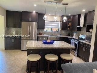 11511 SW 90th Terrace, Miami, FL 33176 Kitchen featuring dark cabinetry, a central island with stone-finish countertops, a stainless steel apron-front sink, recessed lighting, and a triple-pendant fixture