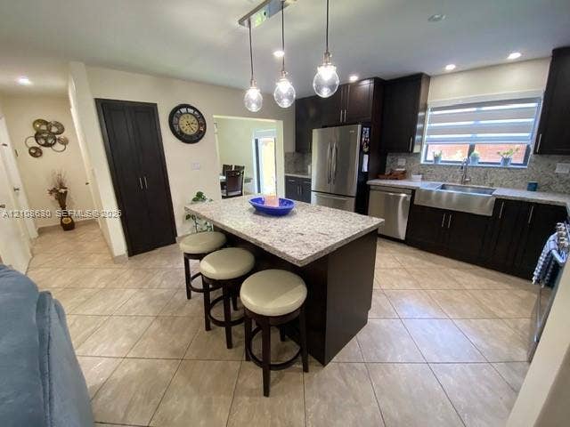 11511 SW 90th Terrace, Miami, FL 33176 Kitchen featuring a central island with a stone-finish countertop, dark wood-finish cabinetry, stainless steel farmhouse-style sink, overhead pendant lighting, and tile flooring