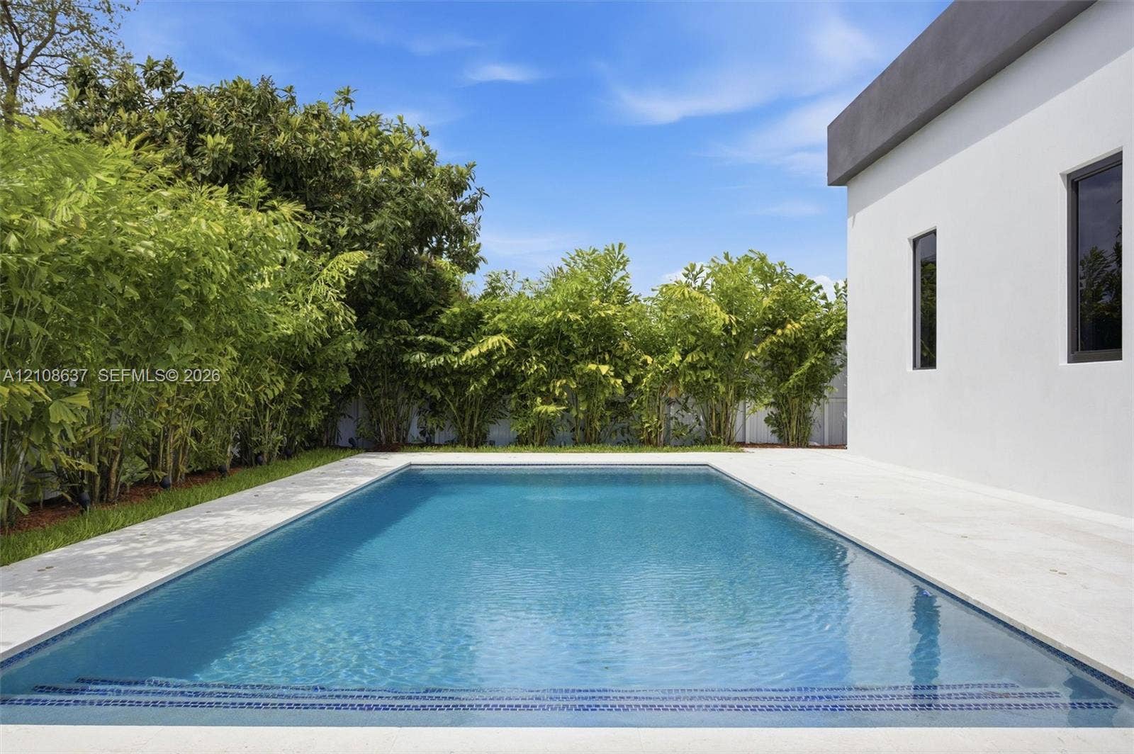 22900 SW 122nd Place, Miami, FL 33170 Rectangular in-ground pool featuring a stone-paver deck, crisp white exterior siding, and dense perimeter landscaping