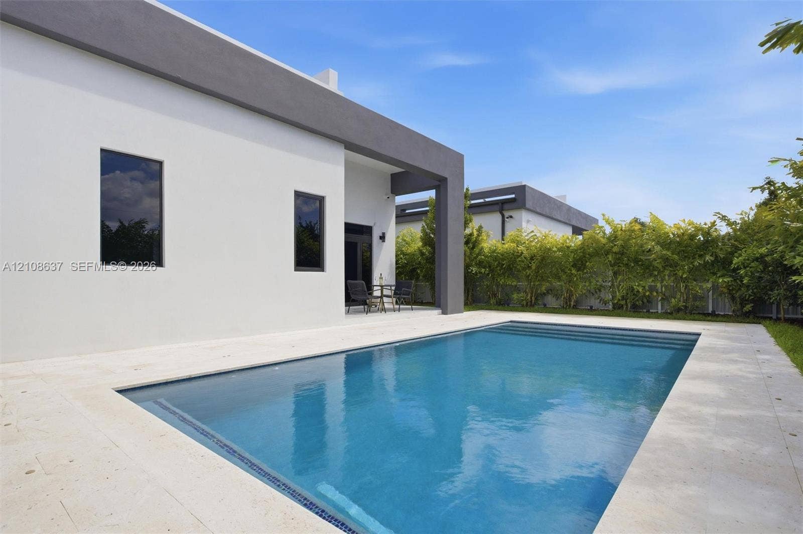 22900 SW 122nd Place, Miami, FL 33170 Modern exterior featuring smooth-finish stucco, a rectangular swimming pool with stone-tile decking, and a covered patio area