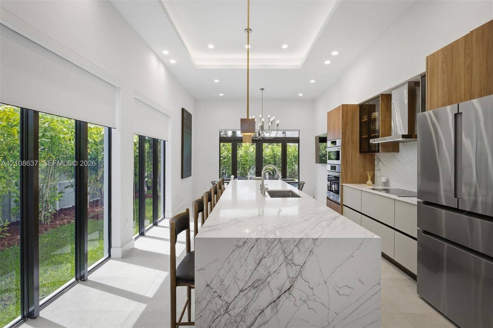 22900 SW 122nd Place, Miami, FL 33170 Kitchen featuring a waterfall-edge island with stone-finish surfaces, custom wood-finish cabinetry, built-in stainless steel appliances, recessed ceiling lighting, and floor-to-ceiling windows
