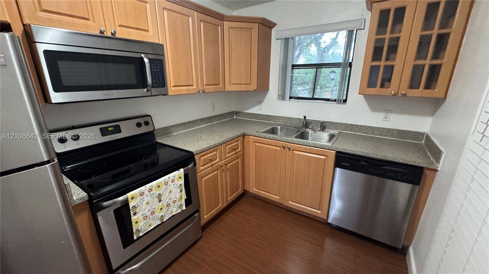 15661 SW 104th Terrace, #3212, Miami, Miami, FL 33196 Kitchen featuring wood cabinetry, stainless steel appliances, speckled stone-composite countertops, a double-basin stainless steel sink, and wood-finish flooring