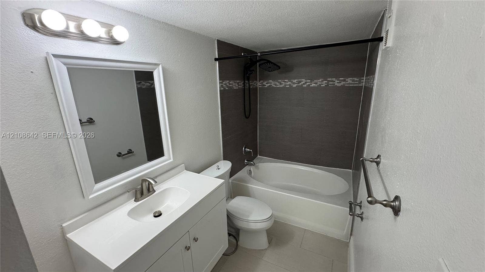 15661 SW 104th Terrace, #3212, Miami, Miami, FL 33196 Bathroom featuring a white vanity cabinet with an integrated basin, a wall-mounted light fixture, and a soaking tub surrounded by dark tile with a decorative accent strip