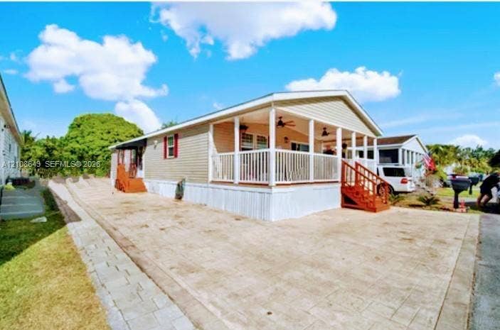 18815 SW 351 Street, Homestead, FL 33034 Exterior facade featuring light-toned horizontal siding, a covered porch with white railing, ceiling fans, and an expansive paved driveway