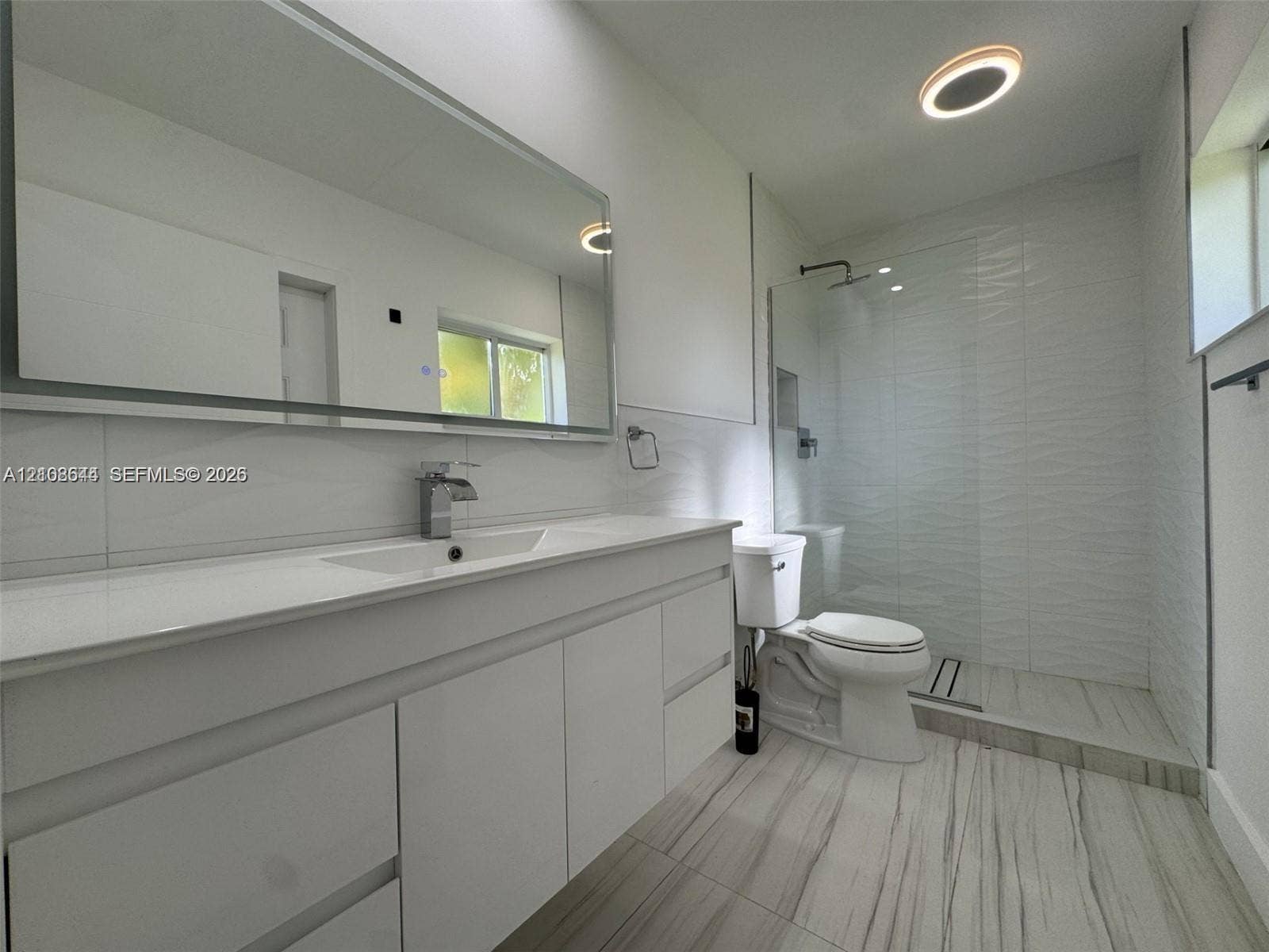 1431 N 14th Way, #rear, Hollywood, Hollywood, FL 33020 Bathroom featuring a large-format white vanity with a rectangular sink, oversized wall-mounted mirror, walk-in glass shower enclosure with textured tile walls, and large-format tile flooring