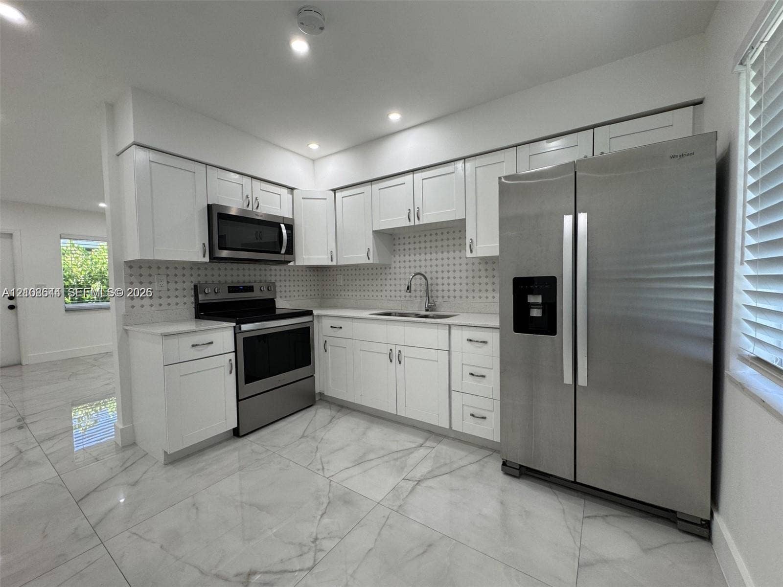 1431 N 14th Way, #rear, Hollywood, Hollywood, FL 33020 Kitchen featuring white shaker-style cabinetry, stainless steel appliances, patterned tile backsplash, light-toned stone-finish flooring, and recessed ceiling lighting