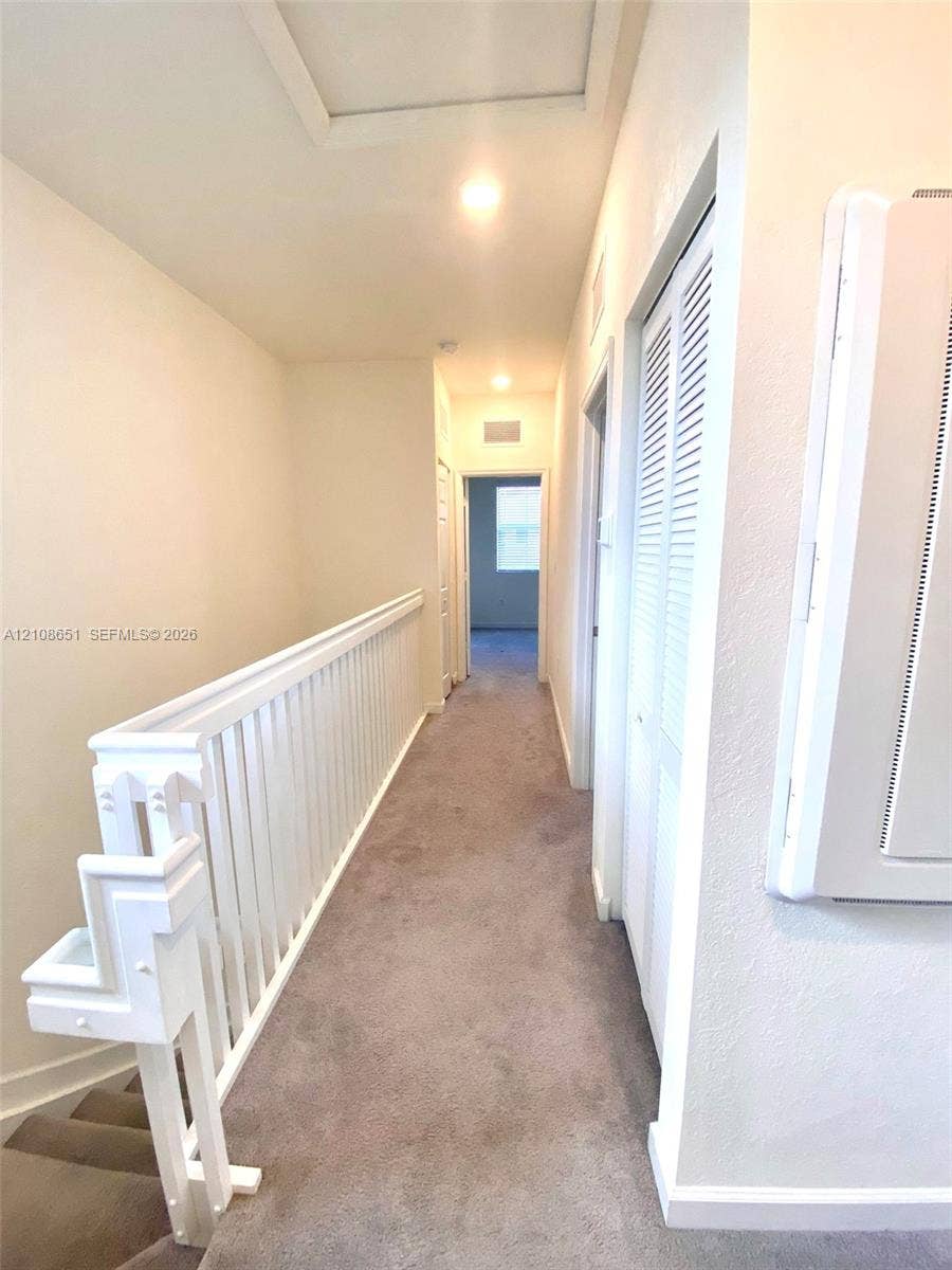 3288 W 106th Terrace, #3288, Hialeah, Hialeah, FL 33018 Hallway featuring neutral carpeting, a white-painted wooden balustrade, and louvered bifold closet doors