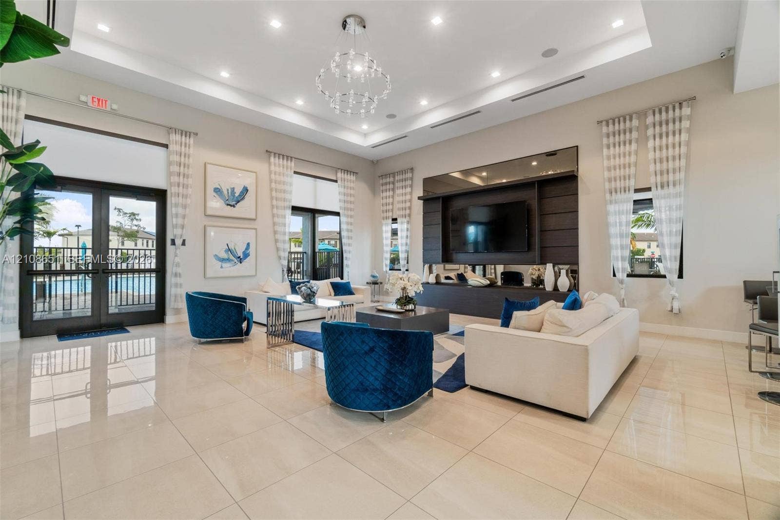 3288 W 106th Terrace, #3288, Hialeah, Hialeah, FL 33018 Open-concept room featuring a tiered tray ceiling, large-format tile flooring, a built-in media wall with integrated shelving, and a multi-tiered crystal chandelier