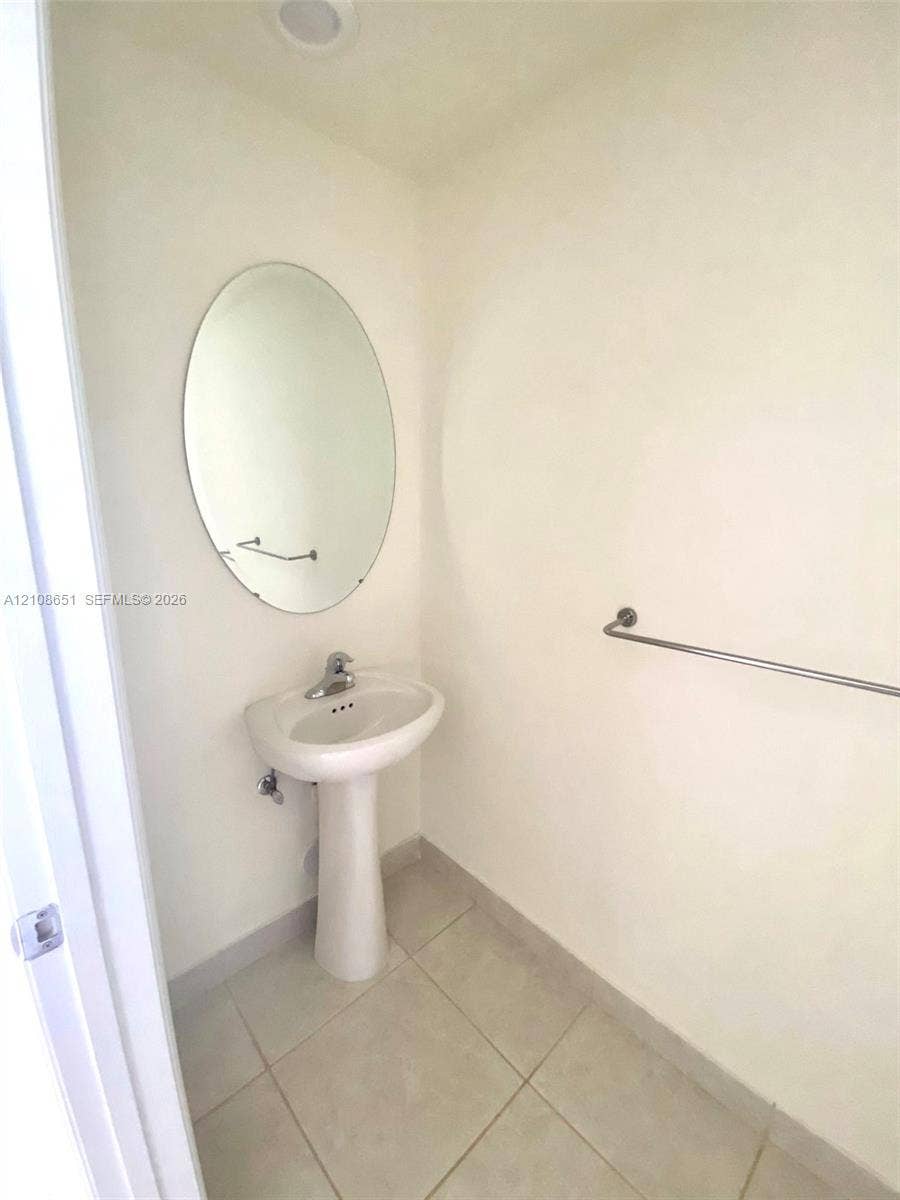 3288 W 106th Terrace, #3288, Hialeah, Hialeah, FL 33018 White pedestal sink with chrome faucet, oval wall-mounted mirror, and neutral-toned tile flooring