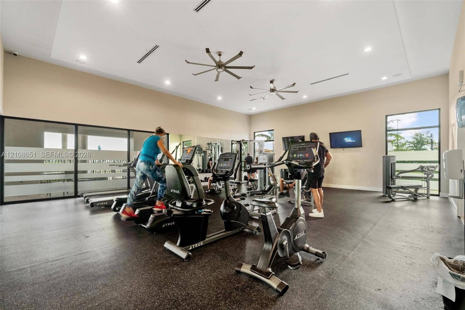 3288 W 106th Terrace, #3288, Hialeah, Hialeah, FL 33018 Fitness facility featuring high ceilings, recessed lighting, dual industrial-style ceiling fans, expansive wall mirrors, and large-format windows with frosted glass detailing