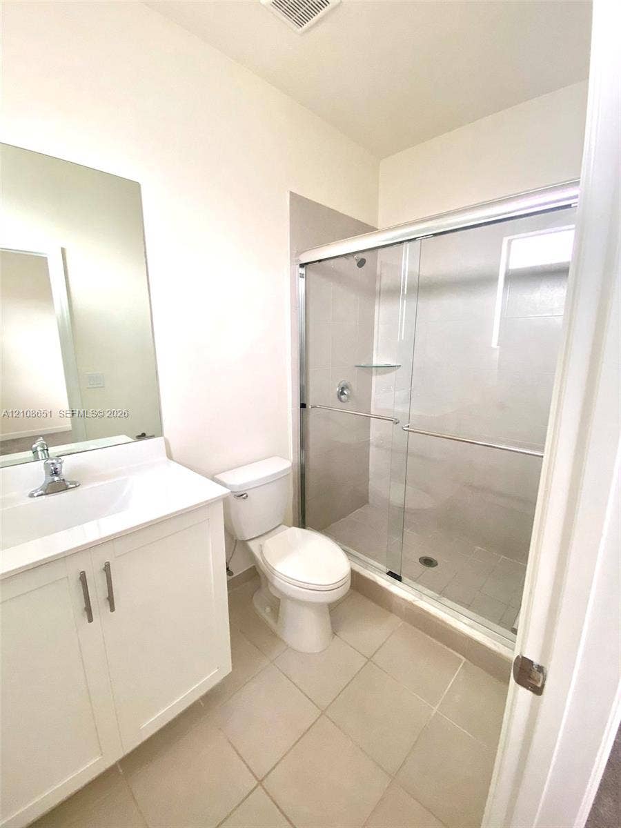 3288 W 106th Terrace, #3288, Hialeah, Hialeah, FL 33018 White vanity featuring a white countertop with integrated sink and chrome faucet, paired with a shower enclosure featuring sliding glass doors and neutral tile flooring