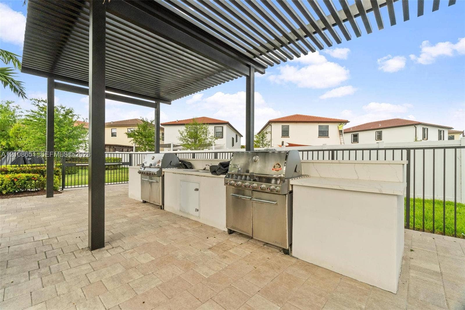 3288 W 106th Terrace, #3288, Hialeah, Hialeah, FL 33018 Outdoor kitchen featuring a stone-topped island, stainless steel grill, integrated storage cabinetry, and a metal pergola overhead, set upon a paved patio
