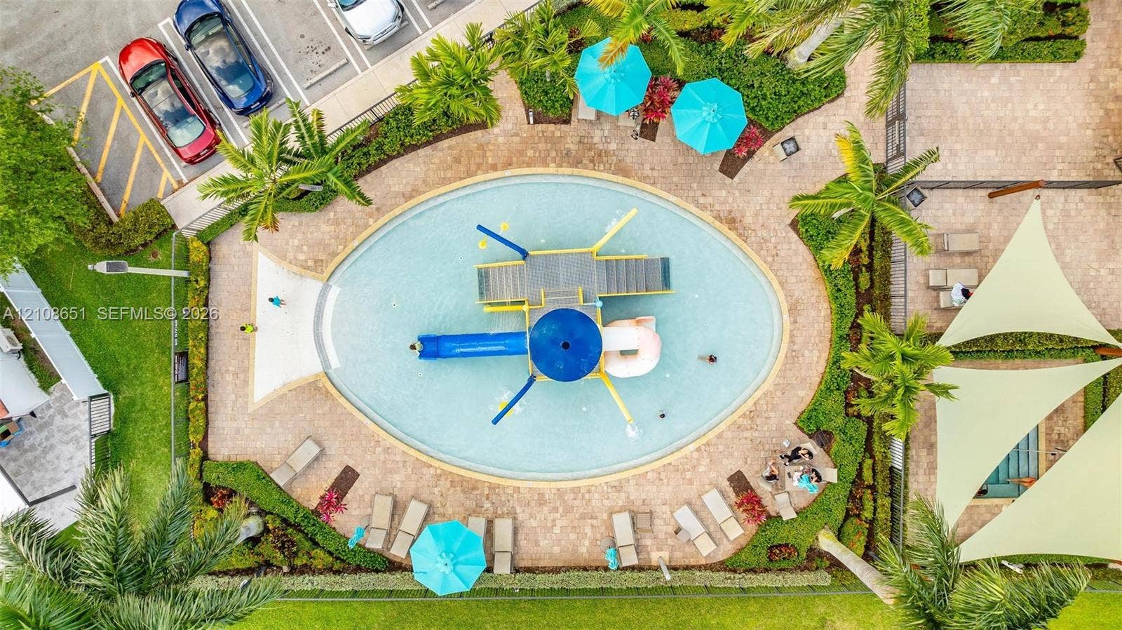 3288 W 106th Terrace, #3288, Hialeah, Hialeah, FL 33018 Oval-shaped swimming pool with a central play structure, integrated slide, paver stone pool deck, and landscaped surroundings