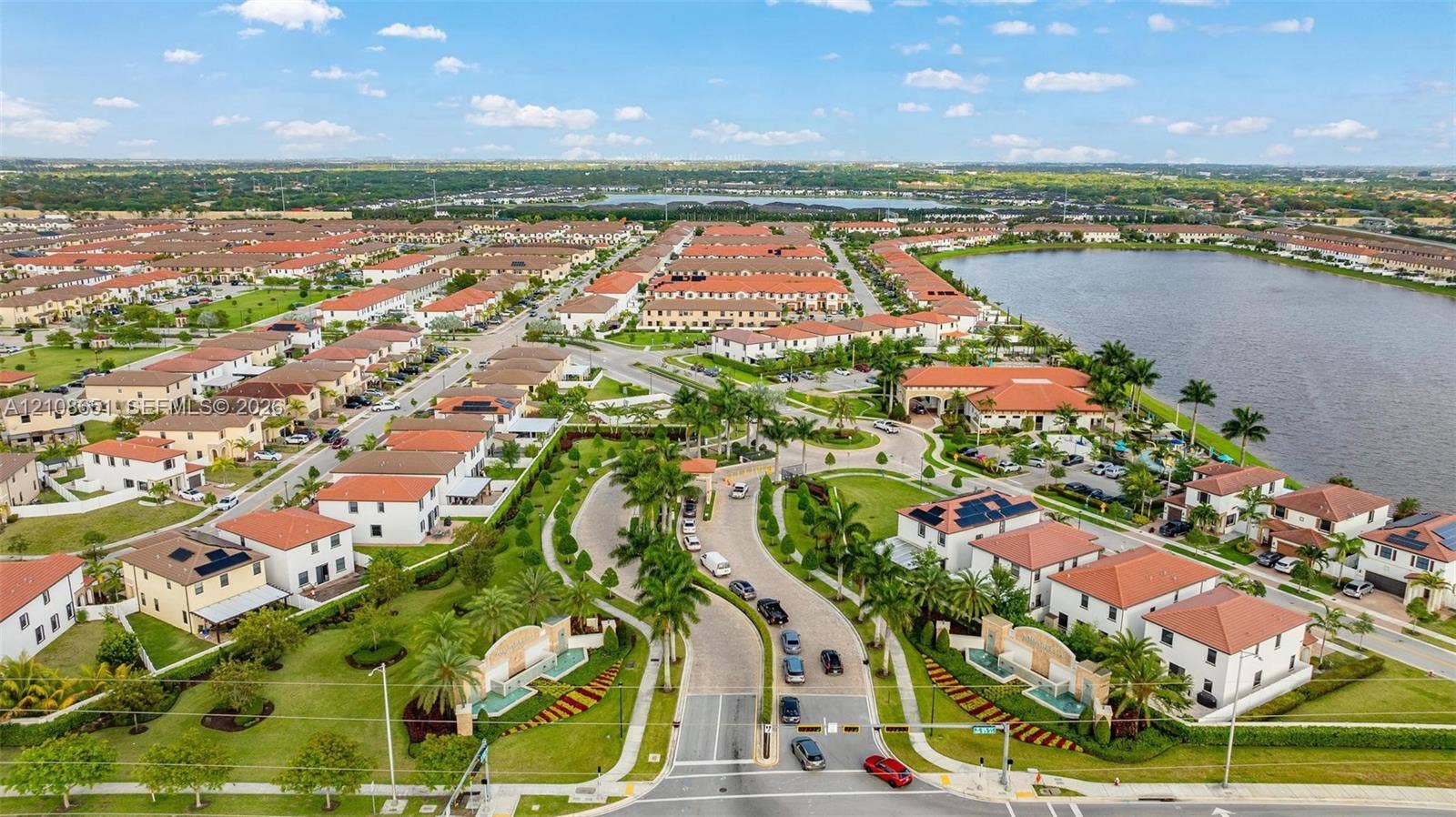 3288 W 106th Terrace, #3288, Hialeah, Hialeah, FL 33018 Aerial view of a residential community featuring red-tile roof architecture, curated landscaping with palm trees, a large lake, and paved roadways with gated access