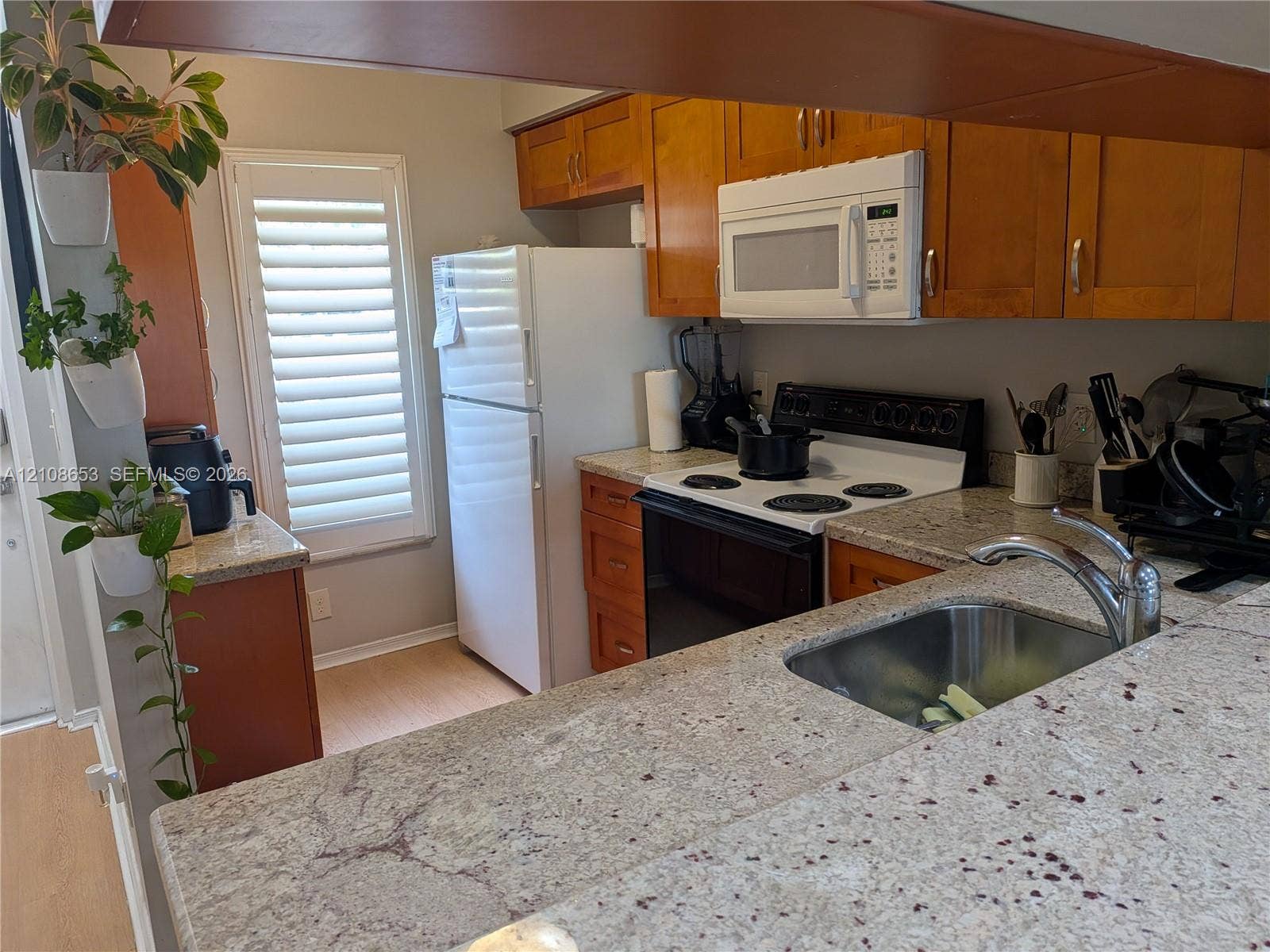 291 Duval Court, #0, Weston, Weston, FL 33326 Kitchen featuring stone-finish countertops, warm-toned wood cabinetry, built-in microwave, stainless steel sink with a high-arch faucet, and shutters covering the window