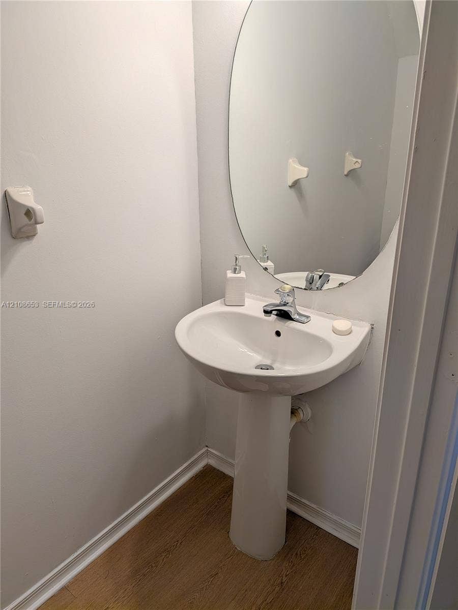 291 Duval Court, #0, Weston, Weston, FL 33326 White ceramic pedestal sink featuring a polished chrome faucet, paired with an oval wall-mounted mirror and wood-finish flooring