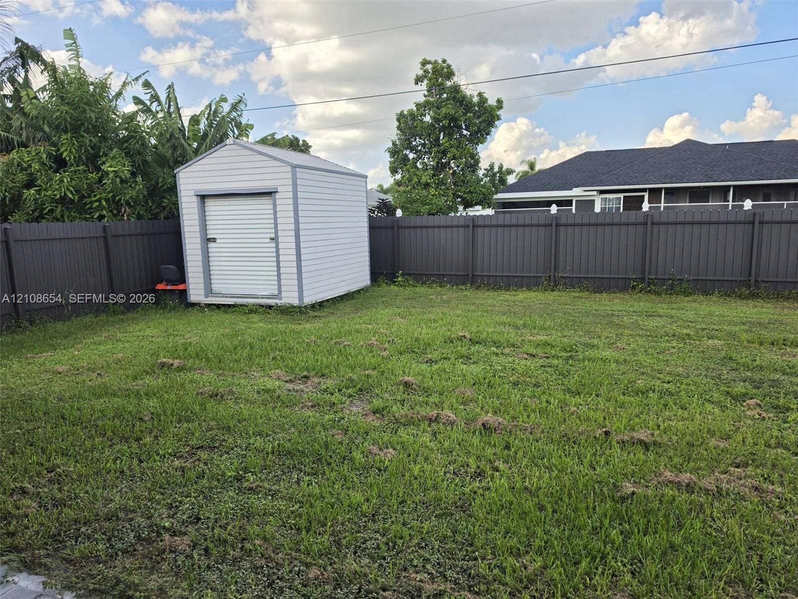 Fenced backyard featuring an expansive lawn and a detached storage shed with a roll-up door