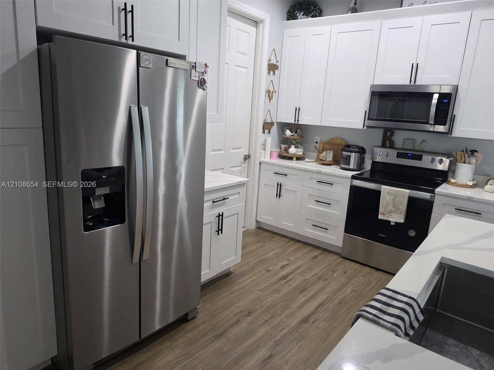 Kitchen featuring white shaker-style cabinetry, stainless steel appliances, quartz countertops, and wood-finish flooring