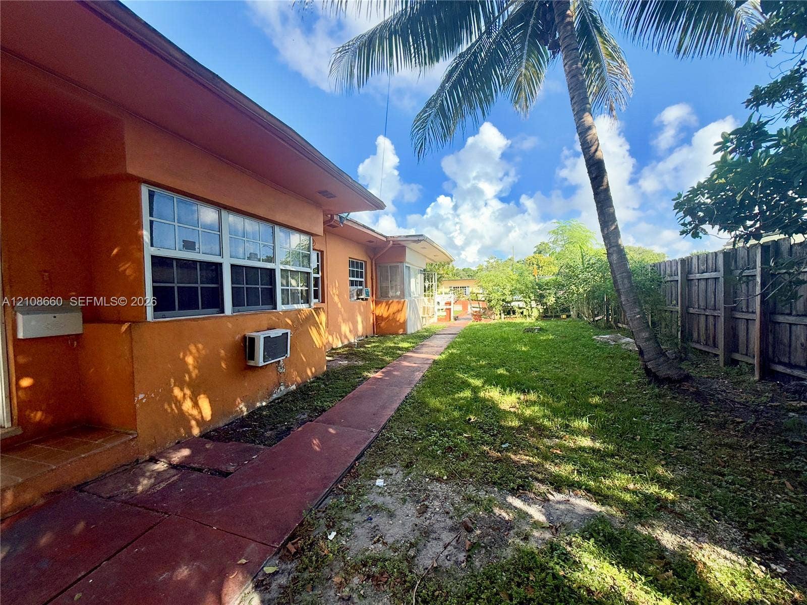262 NE 111th Street, Miami, FL 33161 Side yard featuring a concrete walkway, exterior masonry wall, multi-pane windows, wood-style privacy fencing, and mature palm tree