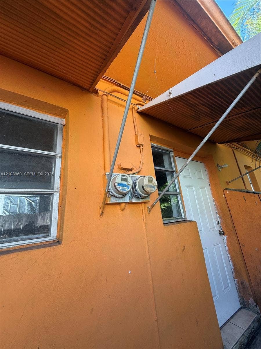 262 NE 111th Street, Miami, FL 33161 Exterior view featuring a stucco finish, dual-panel utility meters, a paneled entry door, and metal awning structures