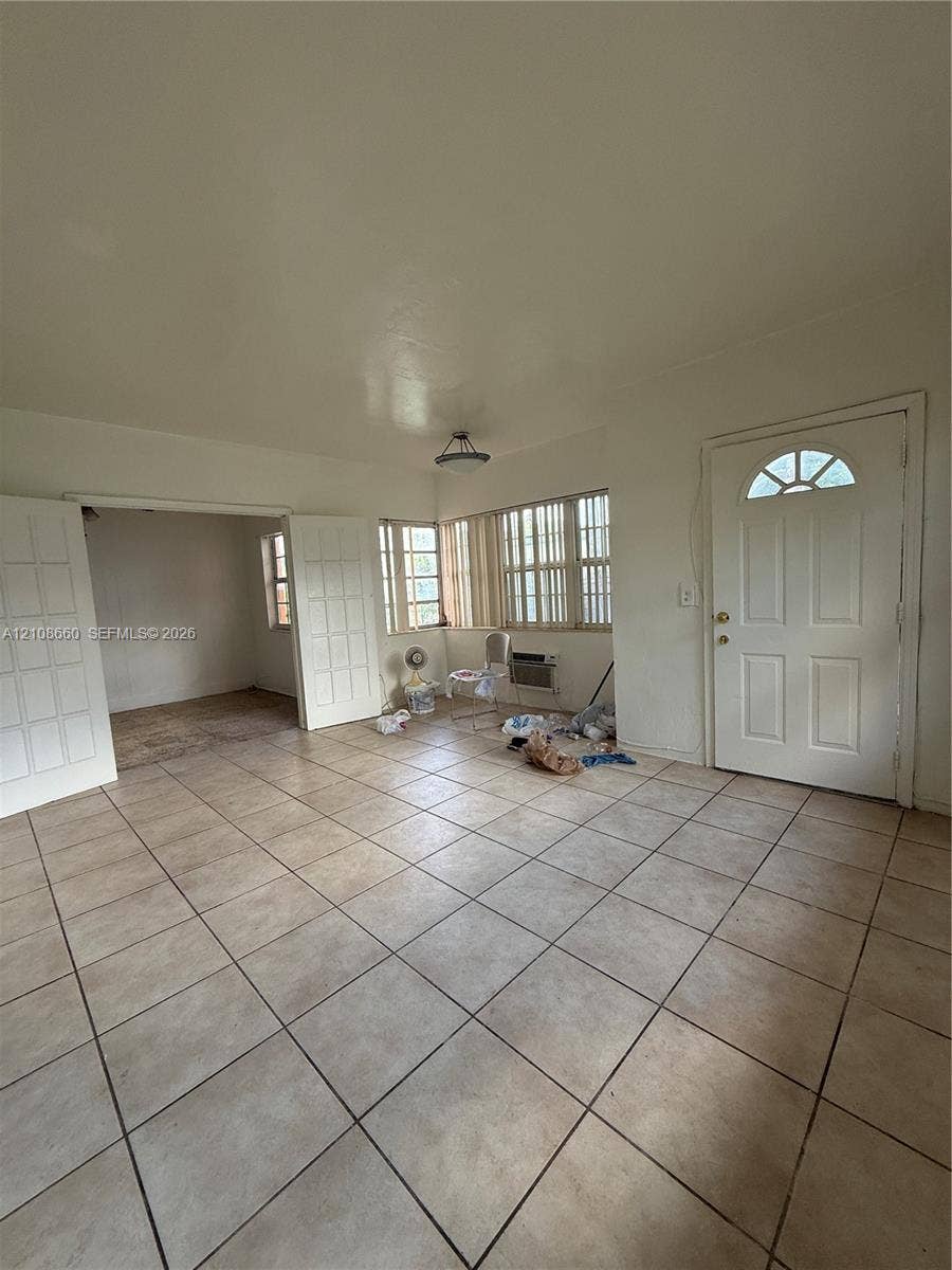 262 NE 111th Street, Miami, FL 33161 Interior space featuring neutral tile flooring, multiple sets of glass-paneled double doors, horizontal window blinds, and an exterior door with an arched glass insert