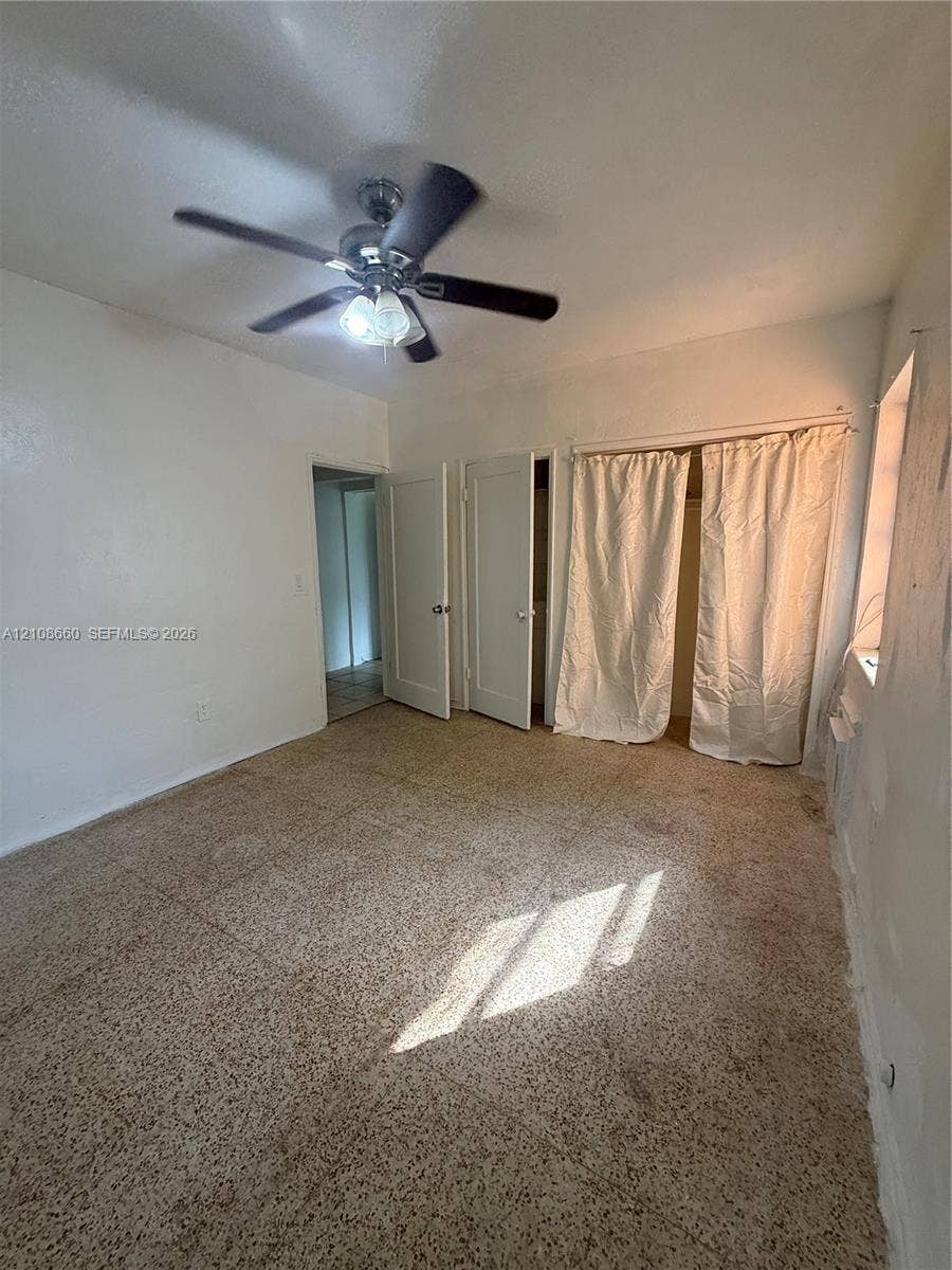 262 NE 111th Street, Miami, FL 33161 Interior space featuring speckled tile flooring, two solid-core doors, and a ceiling-mounted light fixture with a multi-blade fan