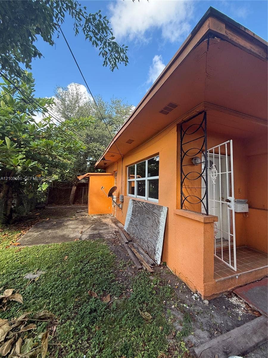262 NE 111th Street, Miami, FL 33161 exterior featuring an attached covered entryway with decorative metal screening, tile porch flooring, and an exterior storage structure