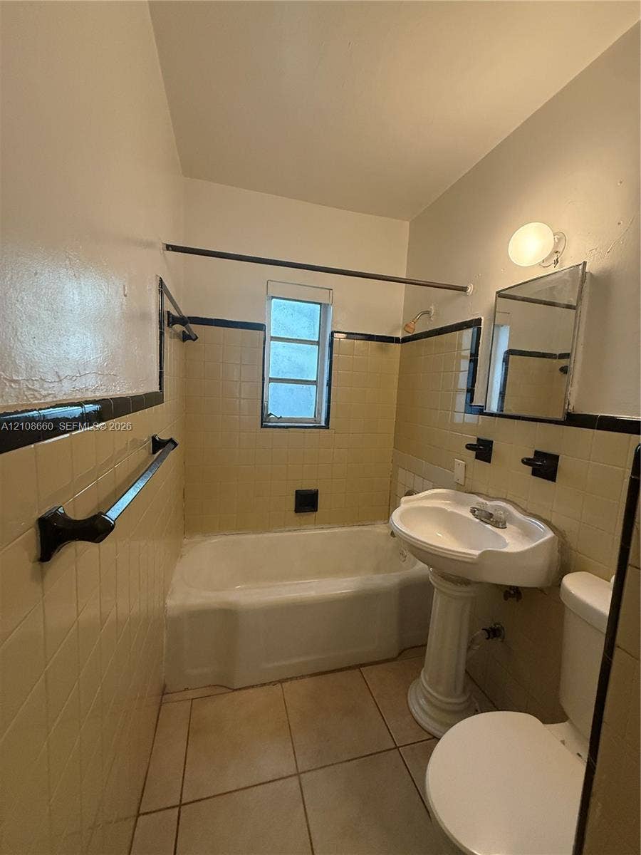 262 NE 111th Street, Miami, FL 33161 Bathroom featuring a pedestal sink, a deep-basin tub with tile surround, black tile accents, and tiled flooring