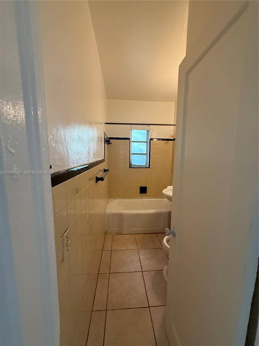 262 NE 111th Street, Miami, FL 33161 Full bathroom featuring tile flooring, a porcelain bathtub, wall-mounted hardware, and decorative tile accent detailing