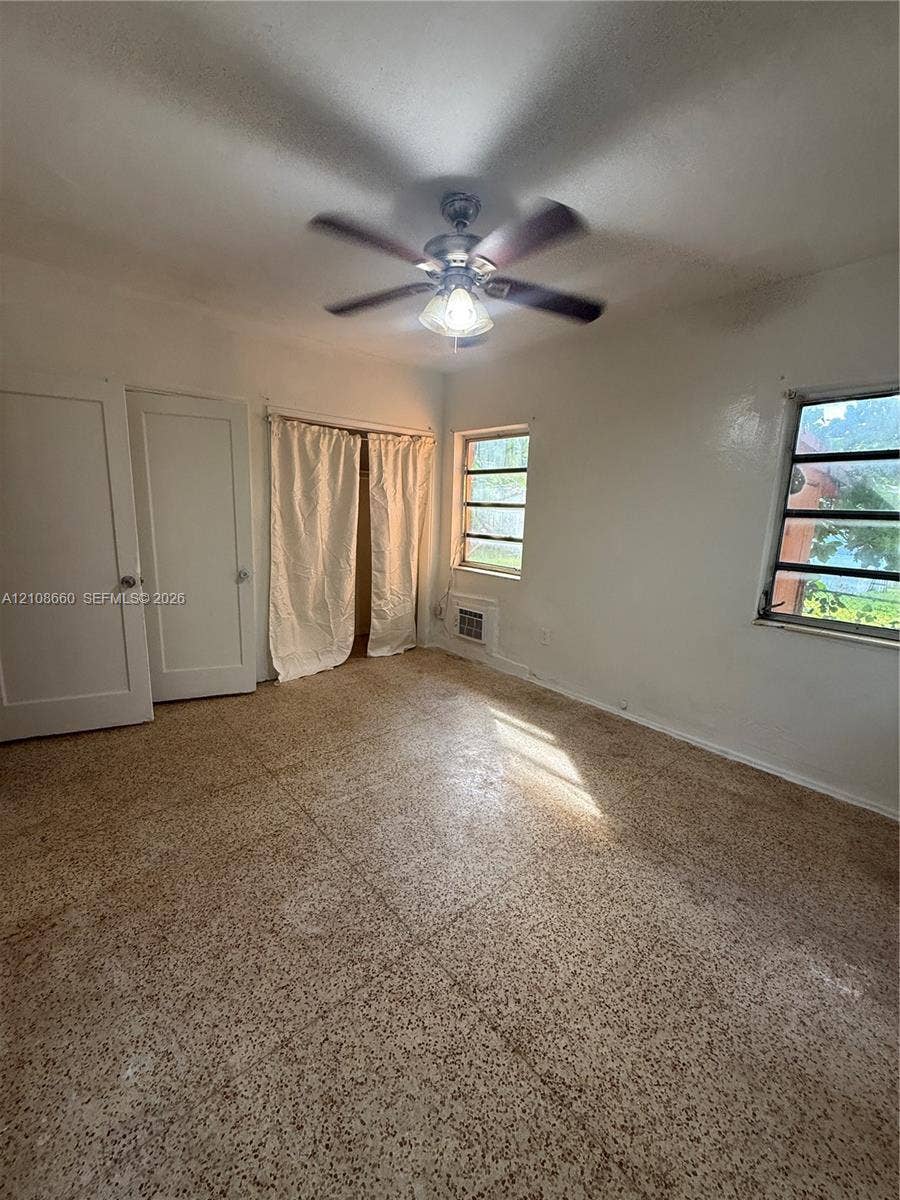 262 NE 111th Street, Miami, FL 33161 Interior space featuring terrazzo flooring, dual-panel doors, horizontal sliding windows, and a ceiling-mounted light fixture with a multi-blade fan