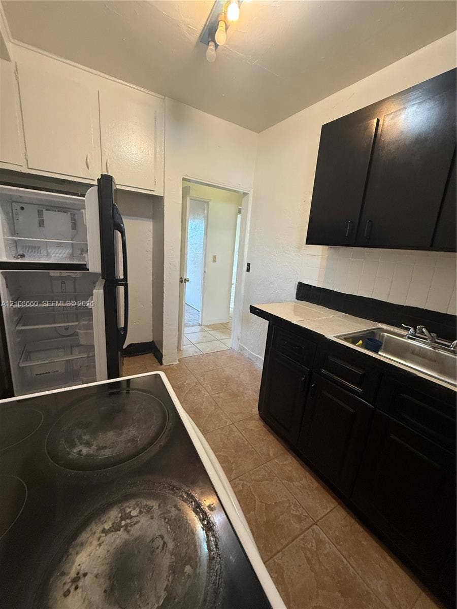 262 NE 111th Street, Miami, FL 33161 Kitchen featuring contrast cabinetry, tiled countertop, stainless steel sink, and ceramic tile flooring