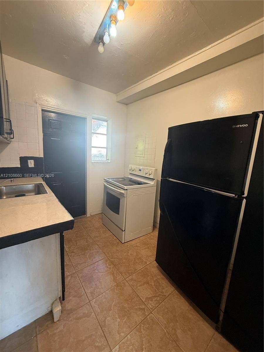 262 NE 111th Street, Miami, FL 33161 Kitchen featuring ceramic tile flooring, a white electric range, a stainless steel sink, and light-toned countertops with dark edging
