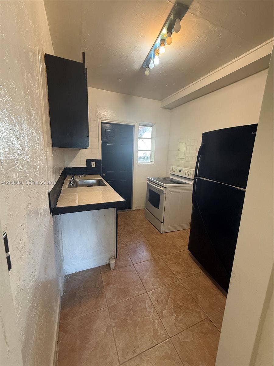 262 NE 111th Street, Miami, FL 33161 Kitchen featuring ceramic tile flooring, built-in cabinetry, tiled backsplash, and stainless steel sink