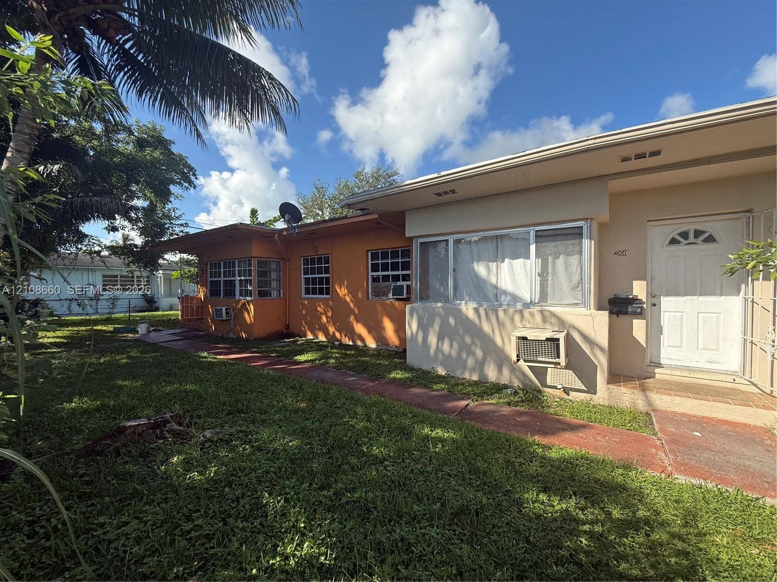 262 NE 111th Street, Miami, FL 33161 Single-story exterior featuring a painted stucco facade, multi-pane windows, a red-toned concrete walkway, and an entry door with a decorative arched window inlay