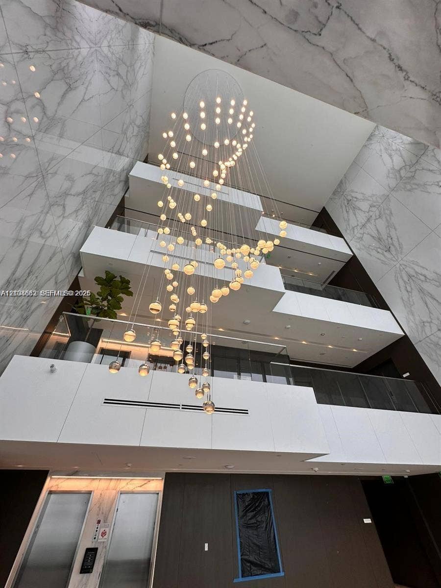 300 Biscayne Boulevard, #2709W, Miami, Miami, FL 33131 Multi-story atrium featuring full-height stone cladding, a tiered geometric balcony design, glass railings, and an expansive multi-globe pendant light fixture