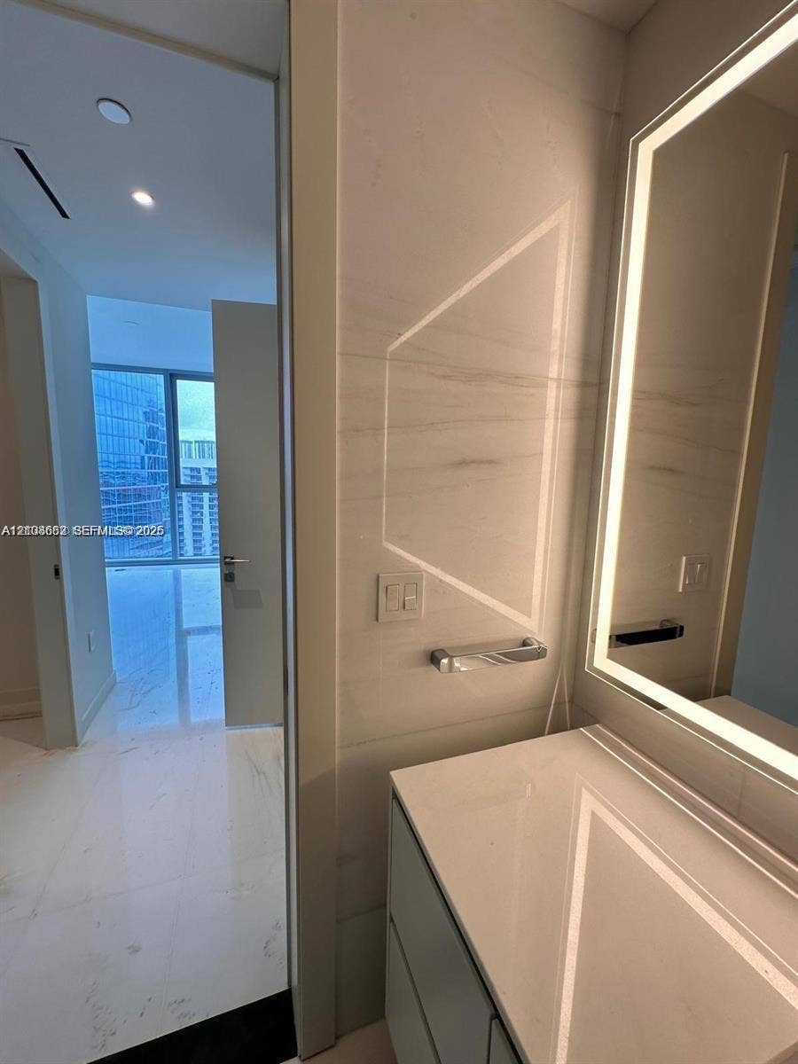 300 Biscayne Boulevard, #2709W, Miami, Miami, FL 33131 Modern vanity featuring a stone countertop, wall-mounted polished chrome hardware, and a backlit mirror, complemented by floor-to-ceiling large-format stone wall cladding