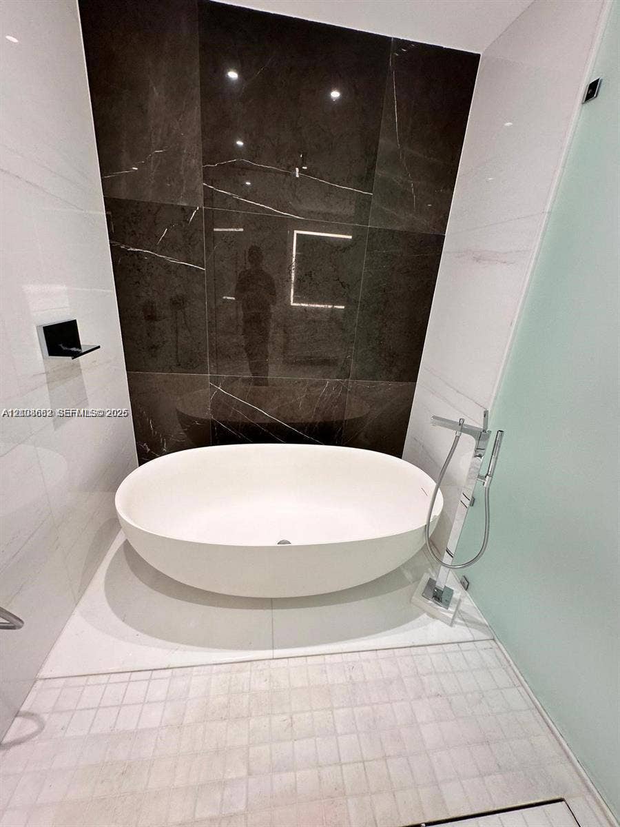 300 Biscayne Boulevard, #2709W, Miami, Miami, FL 33131 Freestanding oval soaking tub featuring a chrome floor-mounted faucet with a handheld sprayer, set against a dark large-format tile accent wall and white wall tile with a glass partition