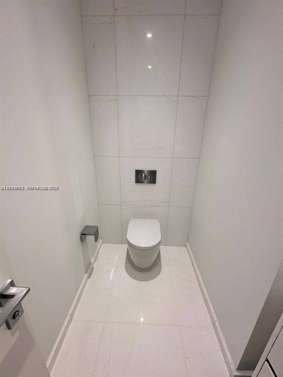 300 Biscayne Boulevard, #2709W, Miami, Miami, FL 33131 Wall-to-wall light-toned tile flooring, floor-to-ceiling tiled accent wall, wall-mounted toilet with a dual-flush actuator, and modern metal hardware