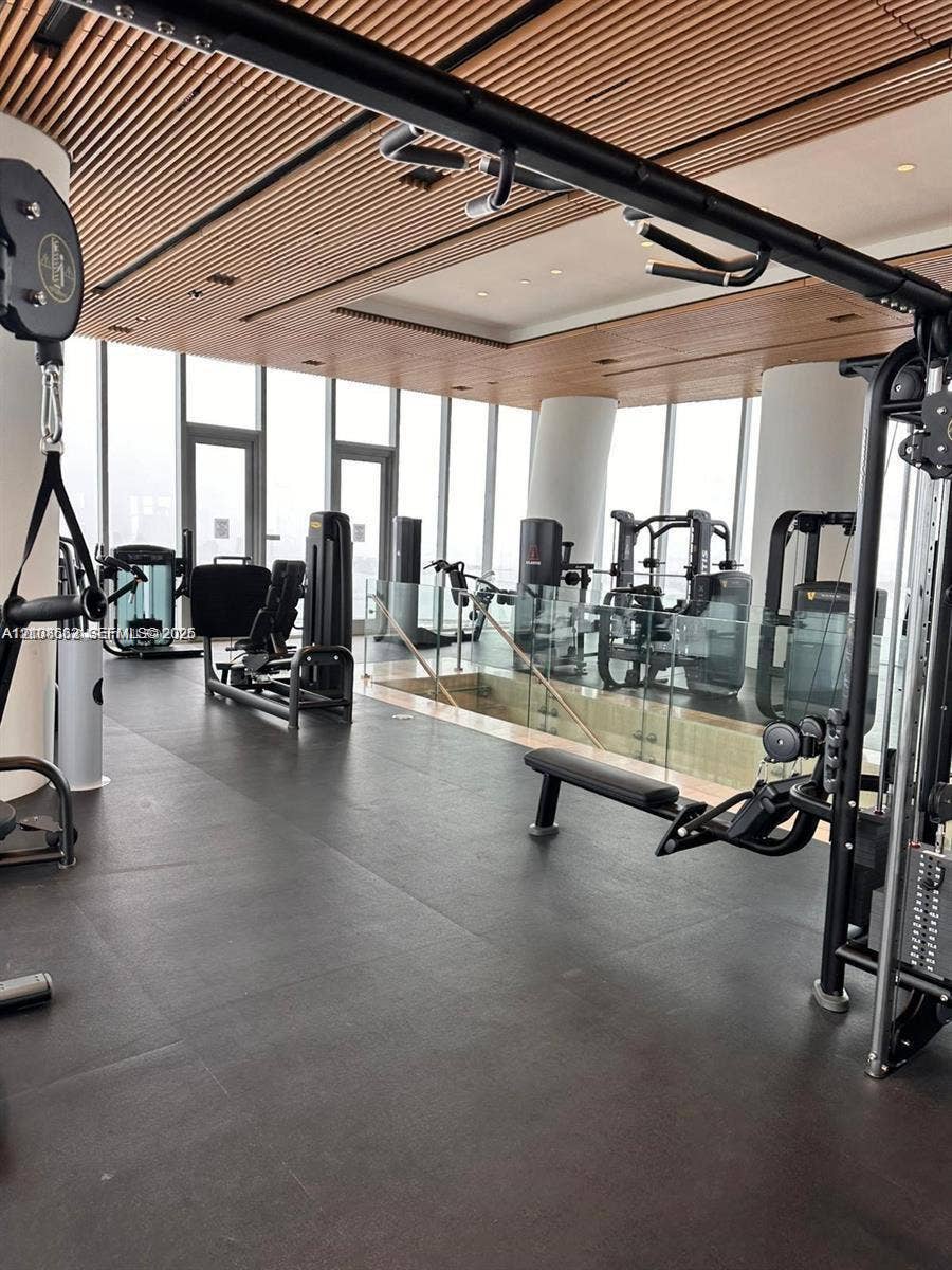 300 Biscayne Boulevard, #2709W, Miami, Miami, FL 33131 Fitness center featuring floor-to-ceiling windows, linear wood-slat ceiling, dark resilient flooring, and glass partition railings