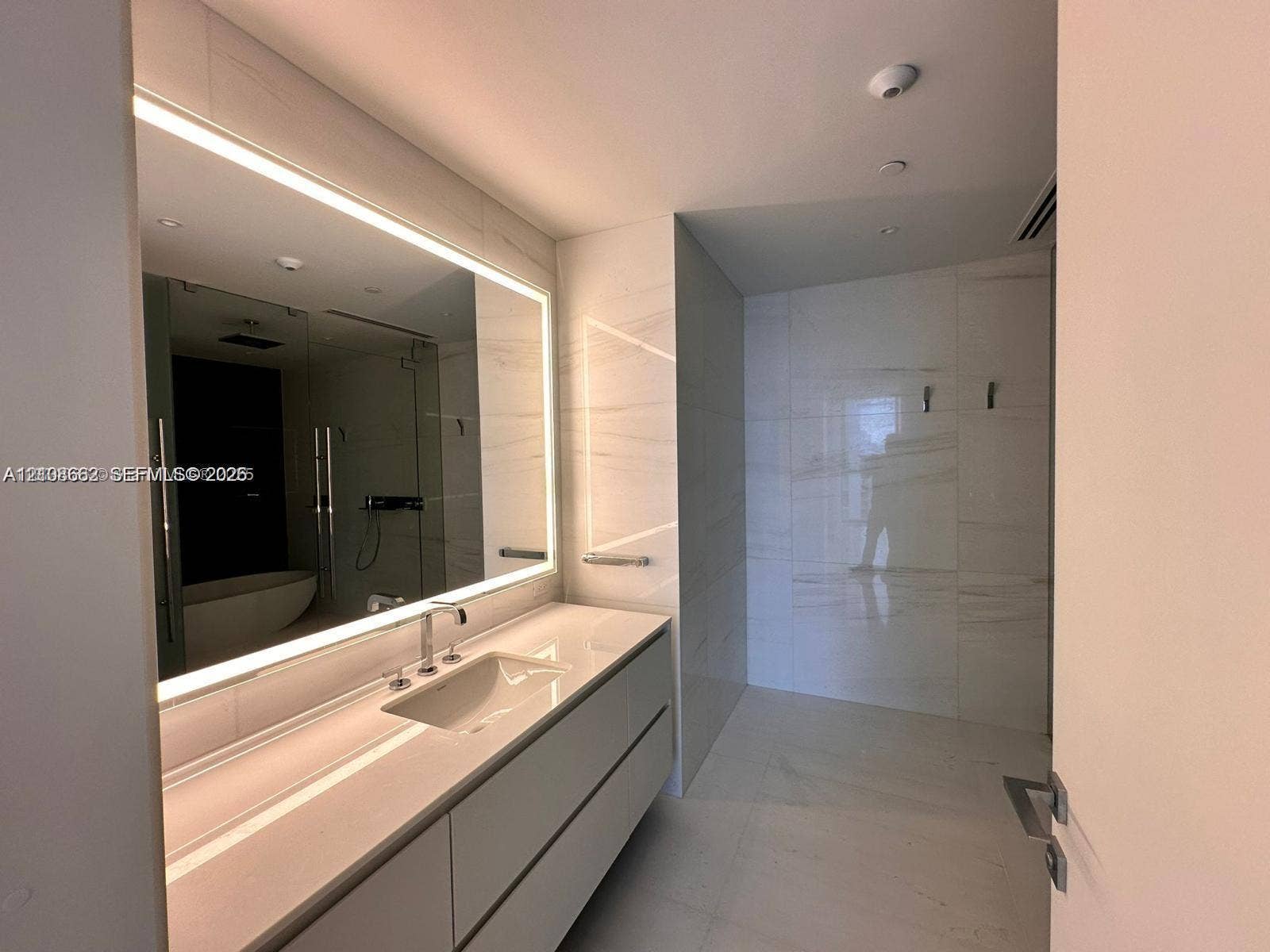 300 Biscayne Boulevard, #2709W, Miami, Miami, FL 33131 Wall-mounted floating vanity with integrated countertop sink, large LED-backlit mirror, and extensive large-format tile wall cladding
