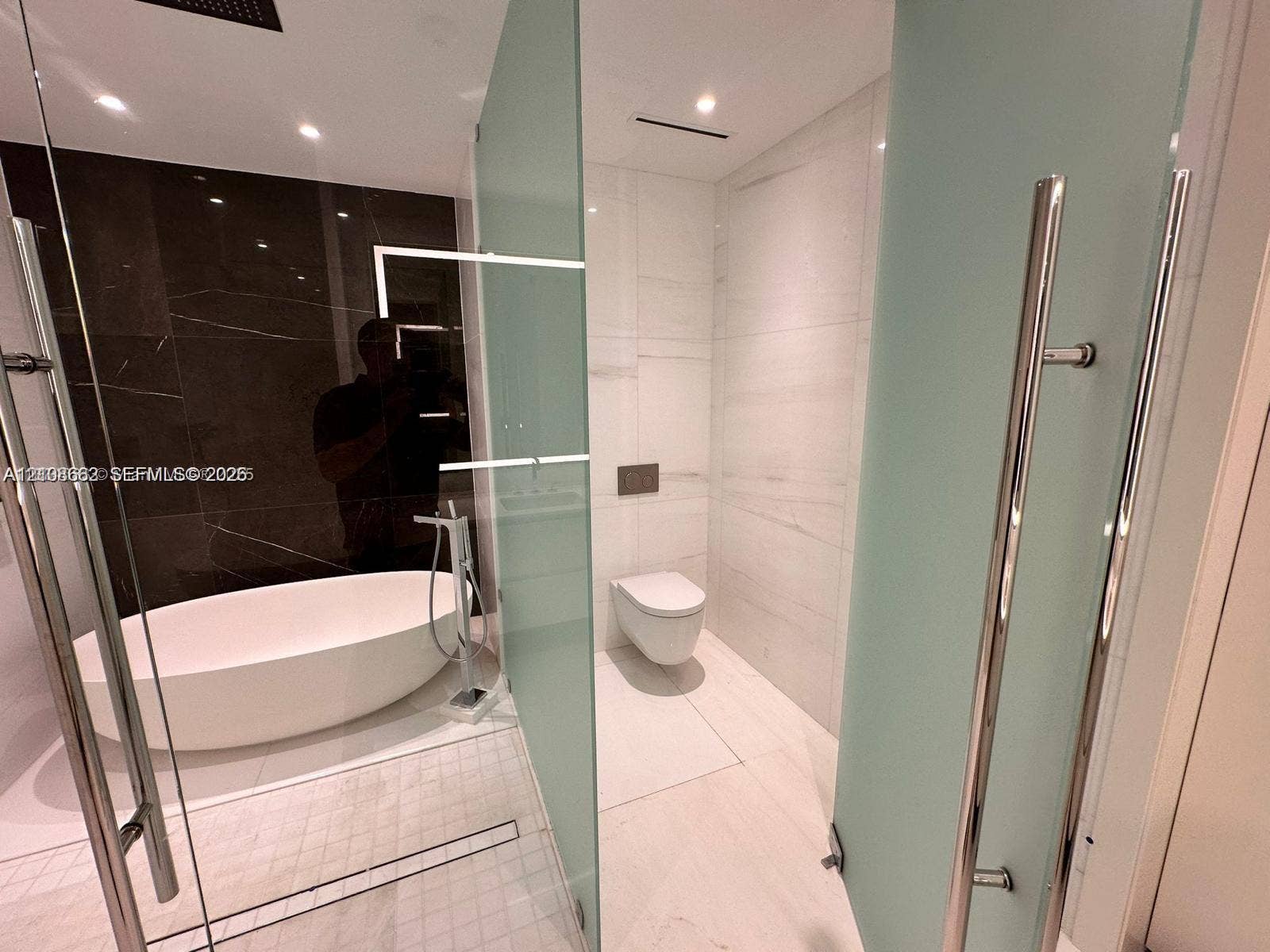 300 Biscayne Boulevard, #2709W, Miami, Miami, FL 33131 Freestanding soaking tub, floor-to-ceiling dark stone-finish wall tile, frosted glass partitions, wall-mounted toilet, and large-format porcelain tile flooring