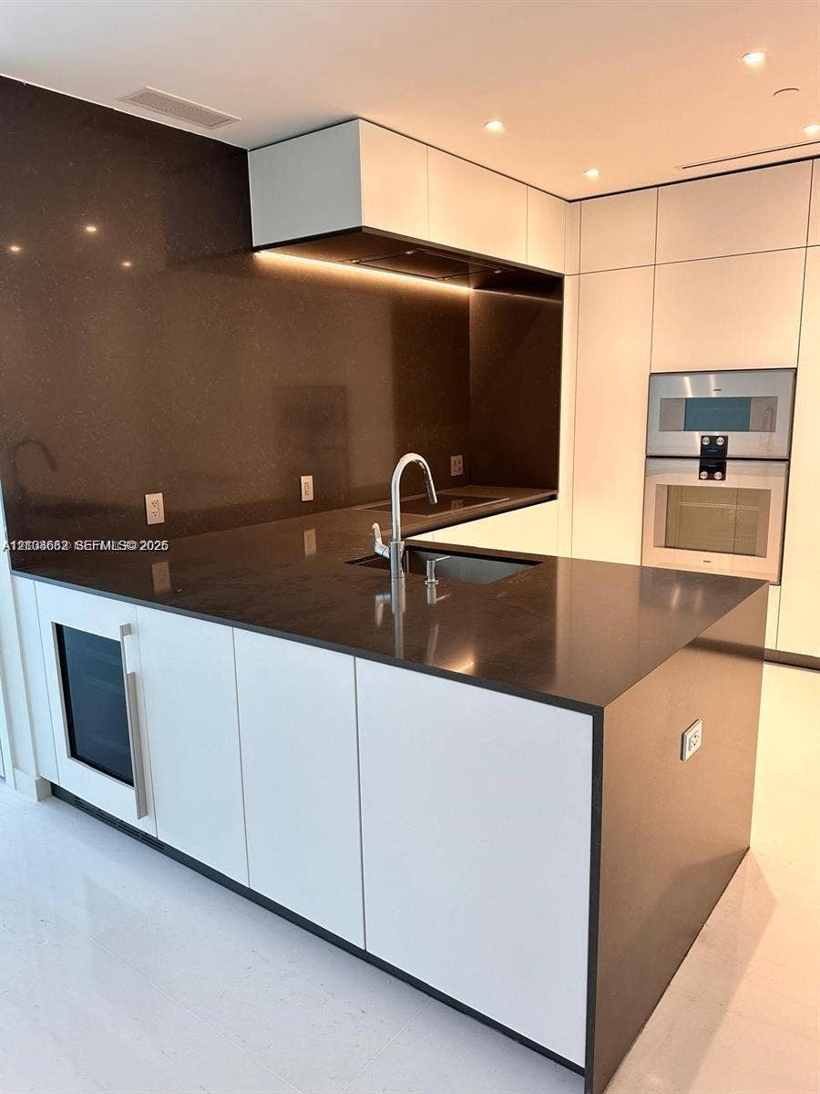 300 Biscayne Boulevard, #2709W, Miami, Miami, FL 33131 Modern kitchen featuring sleek white cabinetry, a dark stone waterfall-edge island, integrated stainless steel appliances, a flush-mount sink with a chrome faucet, and recessed lighting